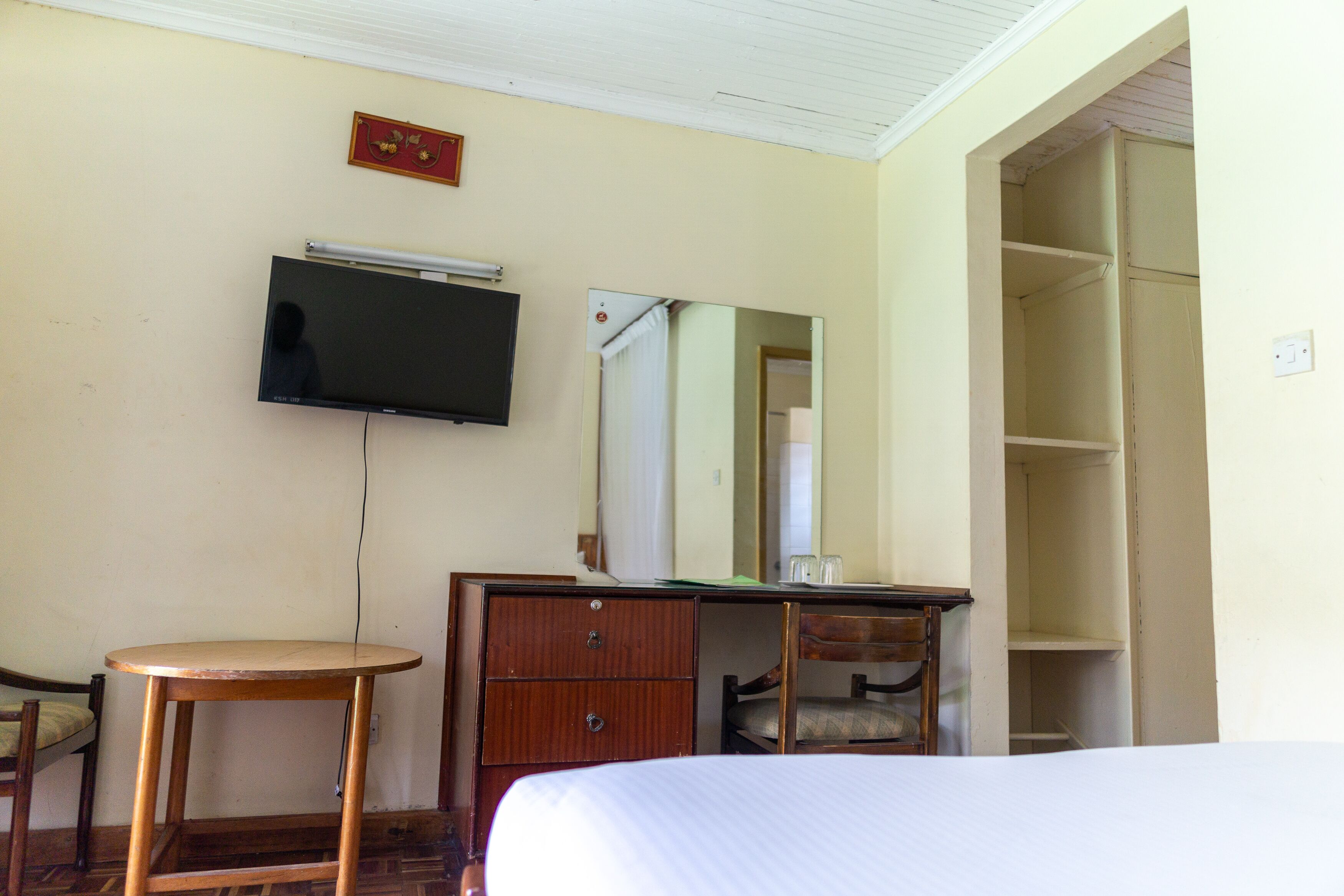 Een hotelkamer met een bed, een houten dressoir, een televisie, een spiegel en een kledingkast.