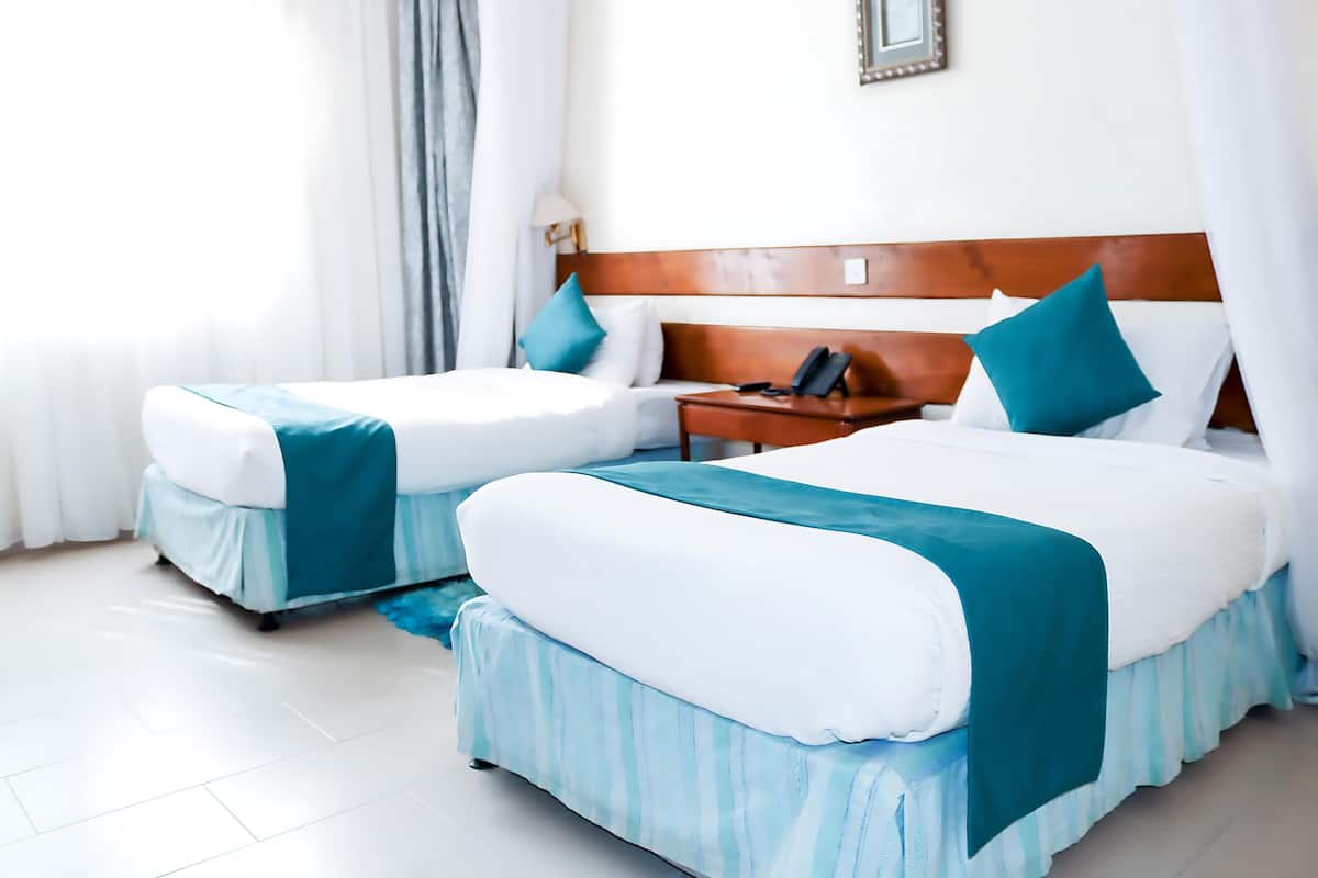 A hotel room with two beds, each with a blue and white bedspread, a wooden headboard, and a bedside table with a lamp.