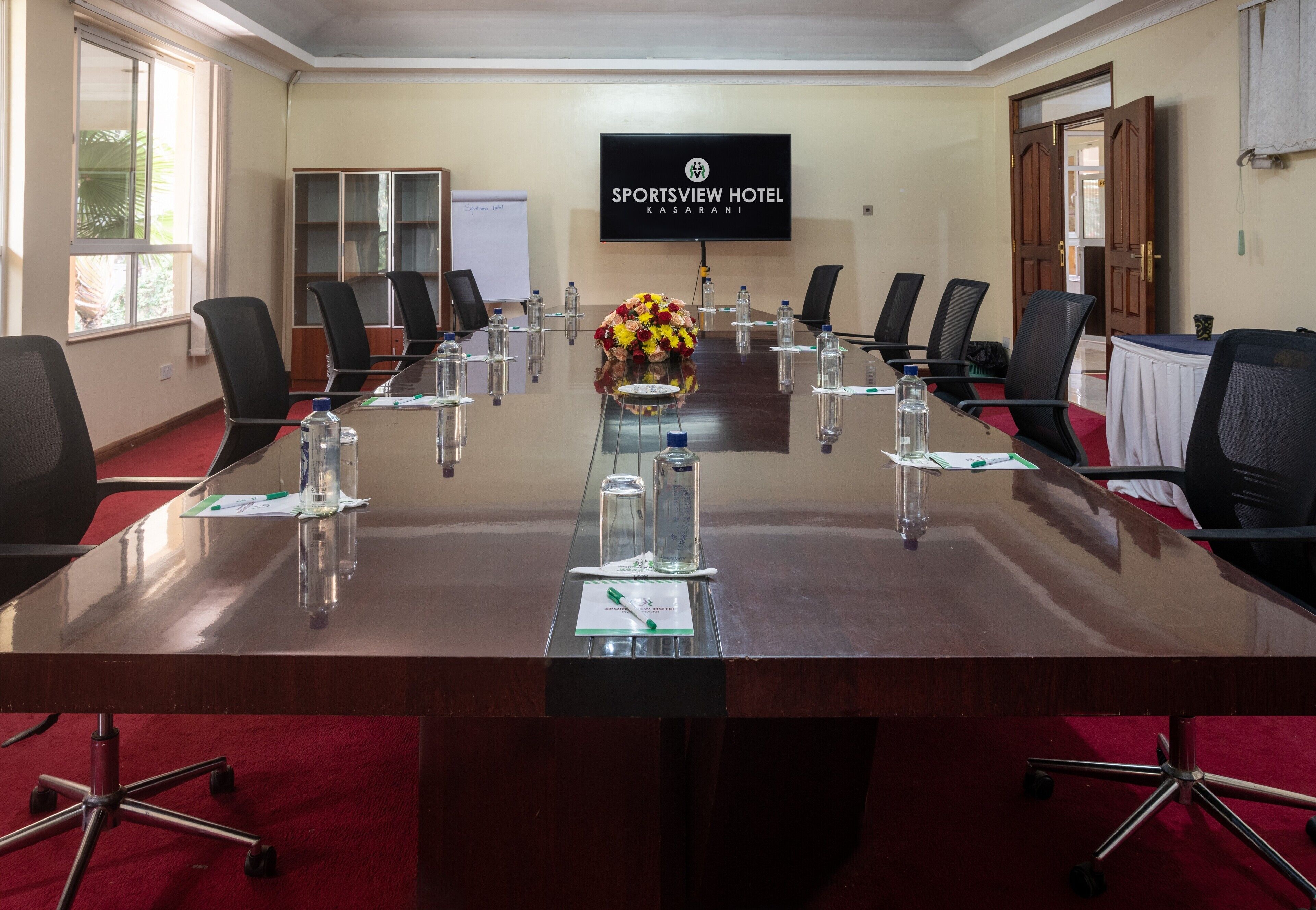 A conference room with a long table, chairs, water bottles, and a floral centerpiece.