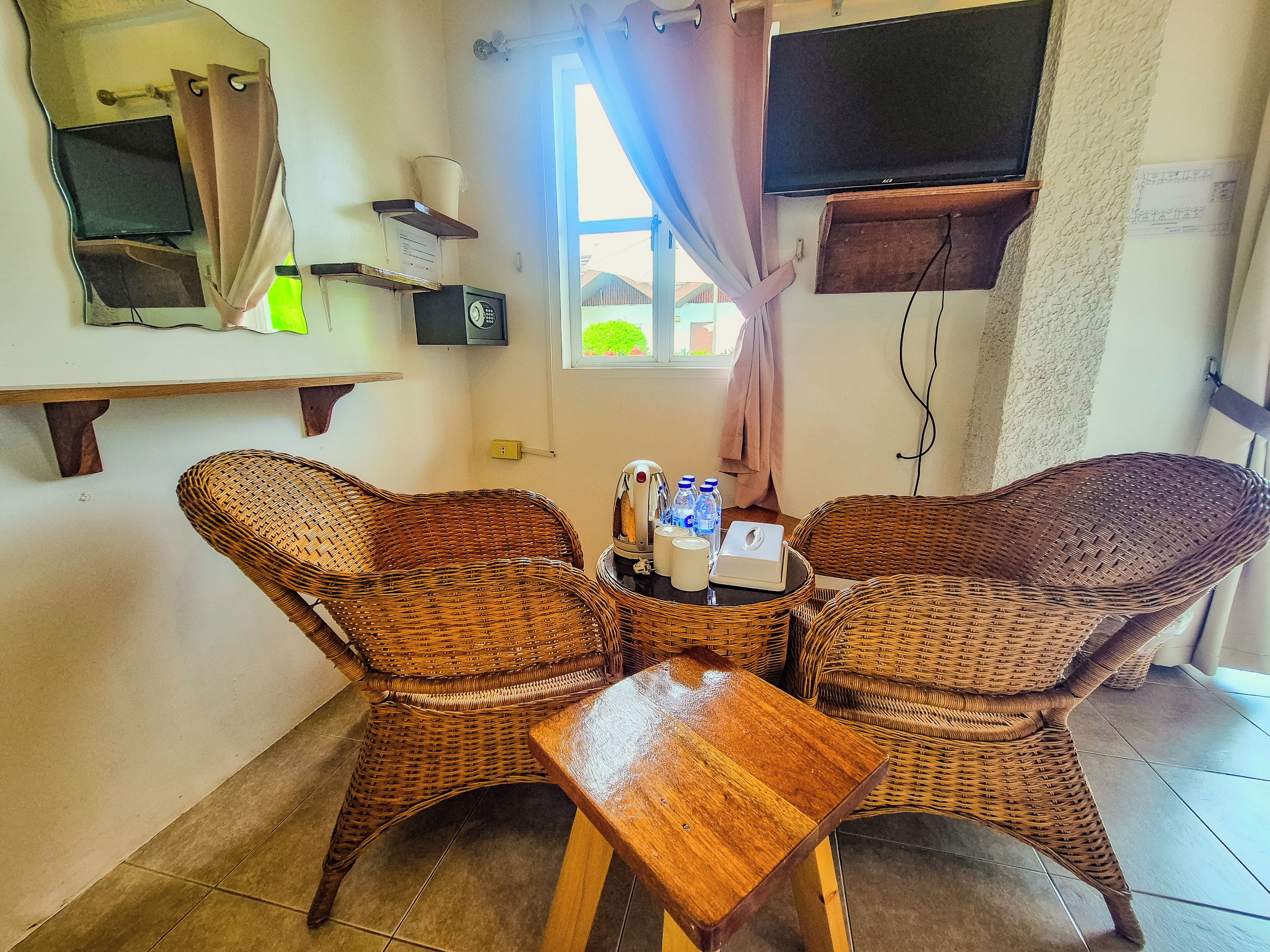 A room with two wicker chairs, a small wooden table, a television, and a window with curtains.
