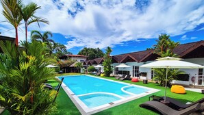 A swimming pool with a green lawn, lounge chairs, and umbrellas. - SunzEn Palawan, Resort (Sunz En Coron Resort) (Coron)