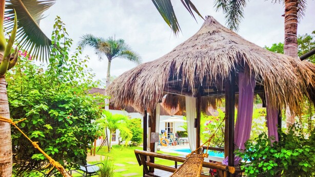 A thatched-roof hut with a hammock in a lush garden. - SunzEn Palawan, Resort (Sunz En Coron Resort) (Coron)