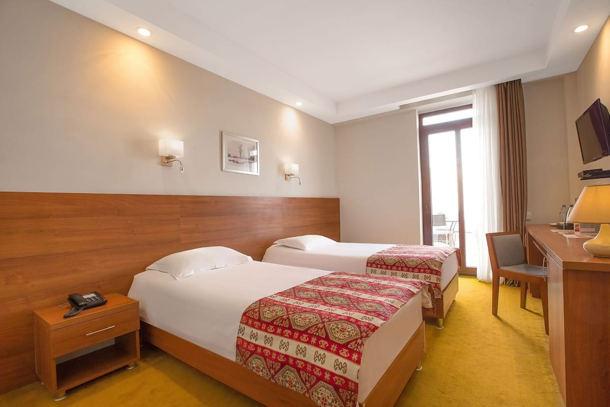 A hotel room with two beds, a desk, a chair, a phone, and a TV.