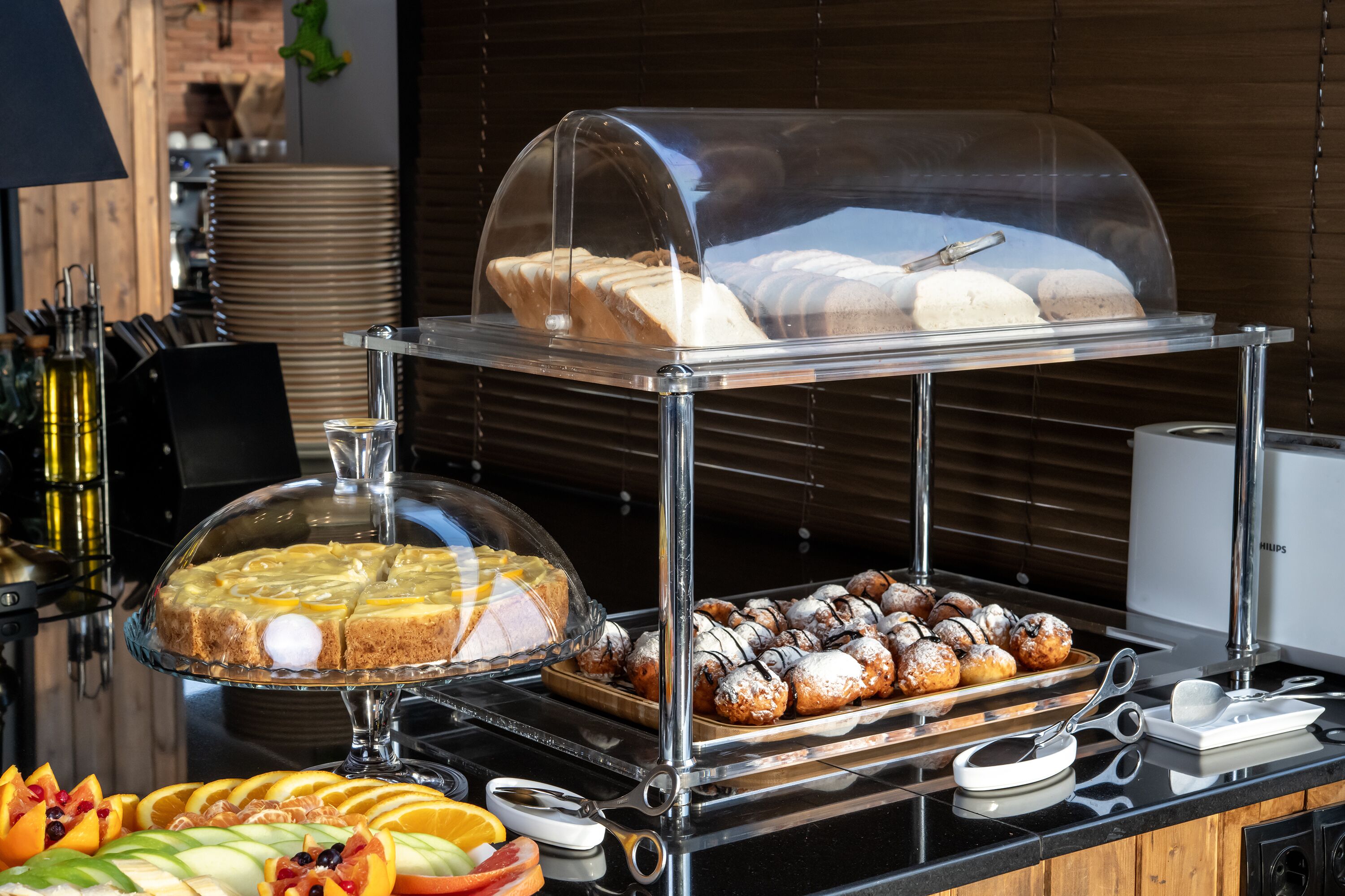 A buffet with various food items including a covered cake, pastries, and fruit.
