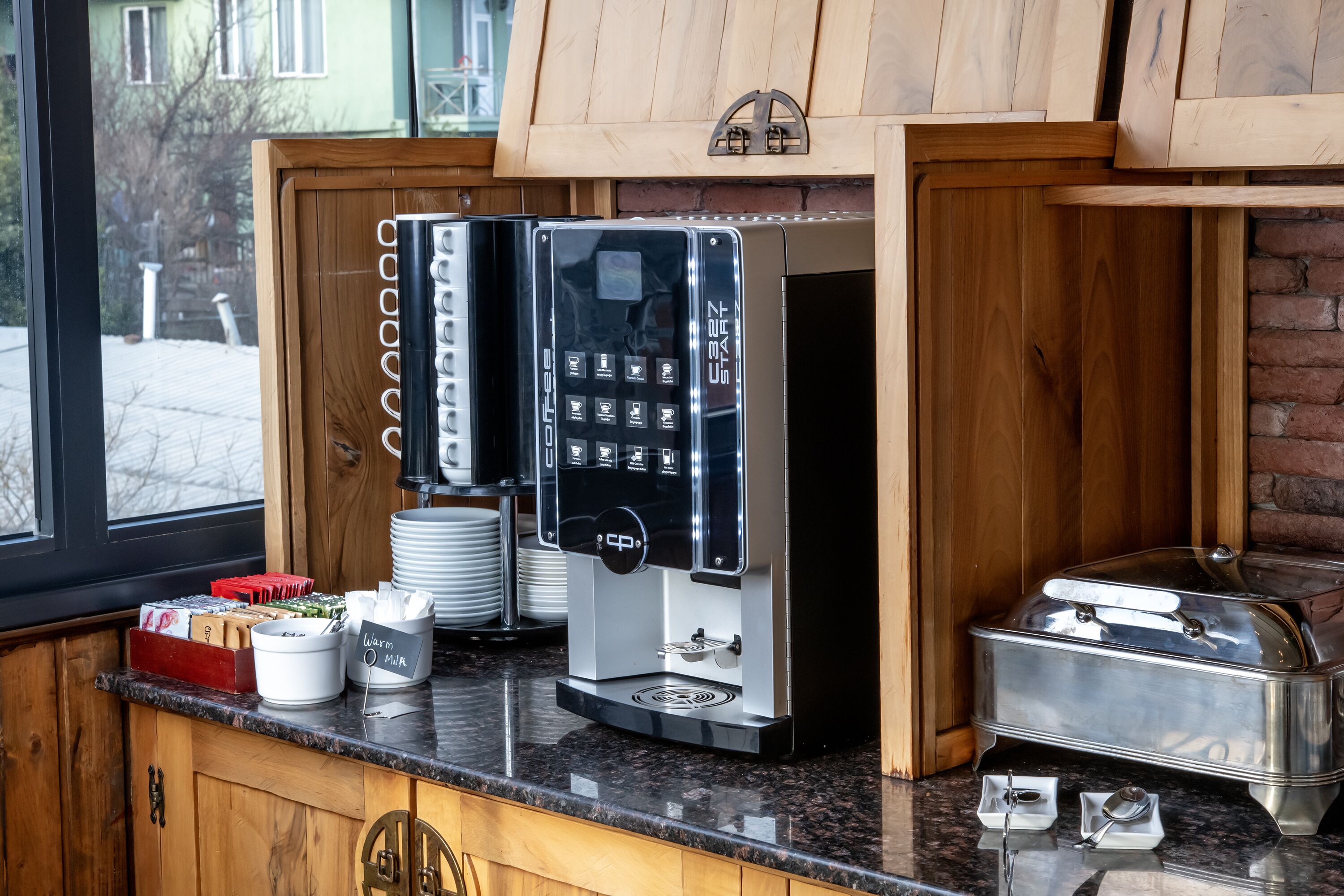 Ein Kaffee-Bereich mit Kaffeemaschine, einem Büfett und Blick ins Freie.