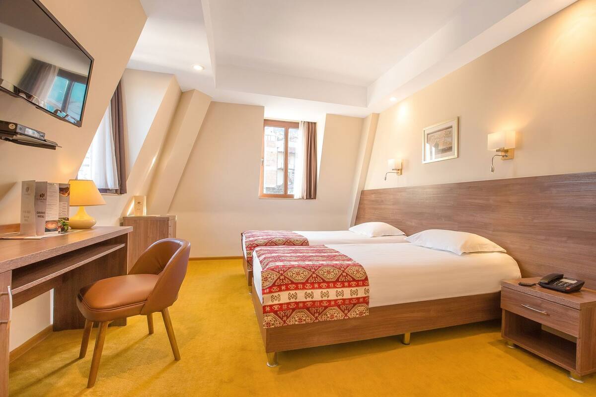 A hotel room with a bed, desk, chair, and a TV.
