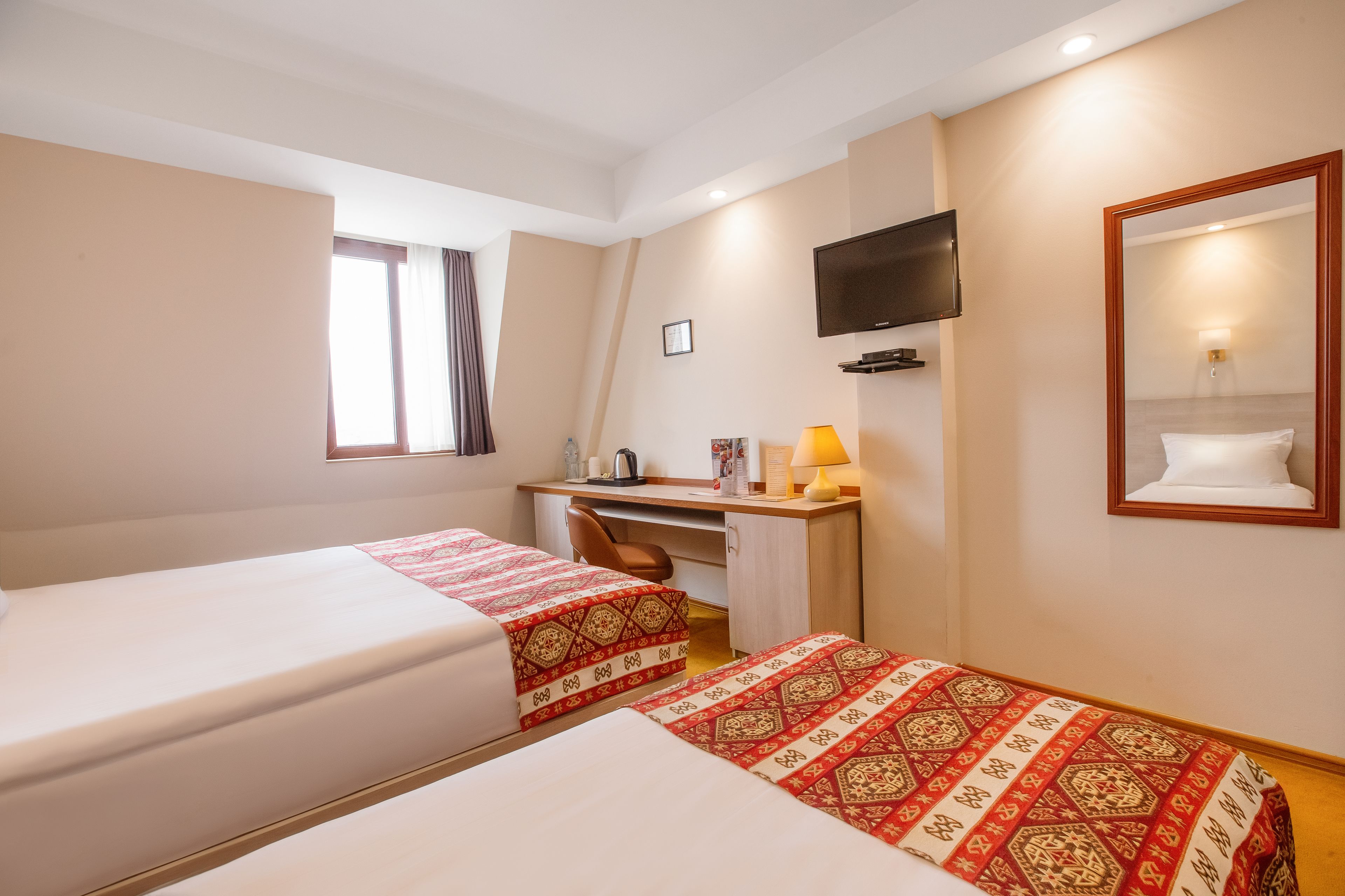 A hotel room with two beds, a desk, a chair, a TV, and a mirror.