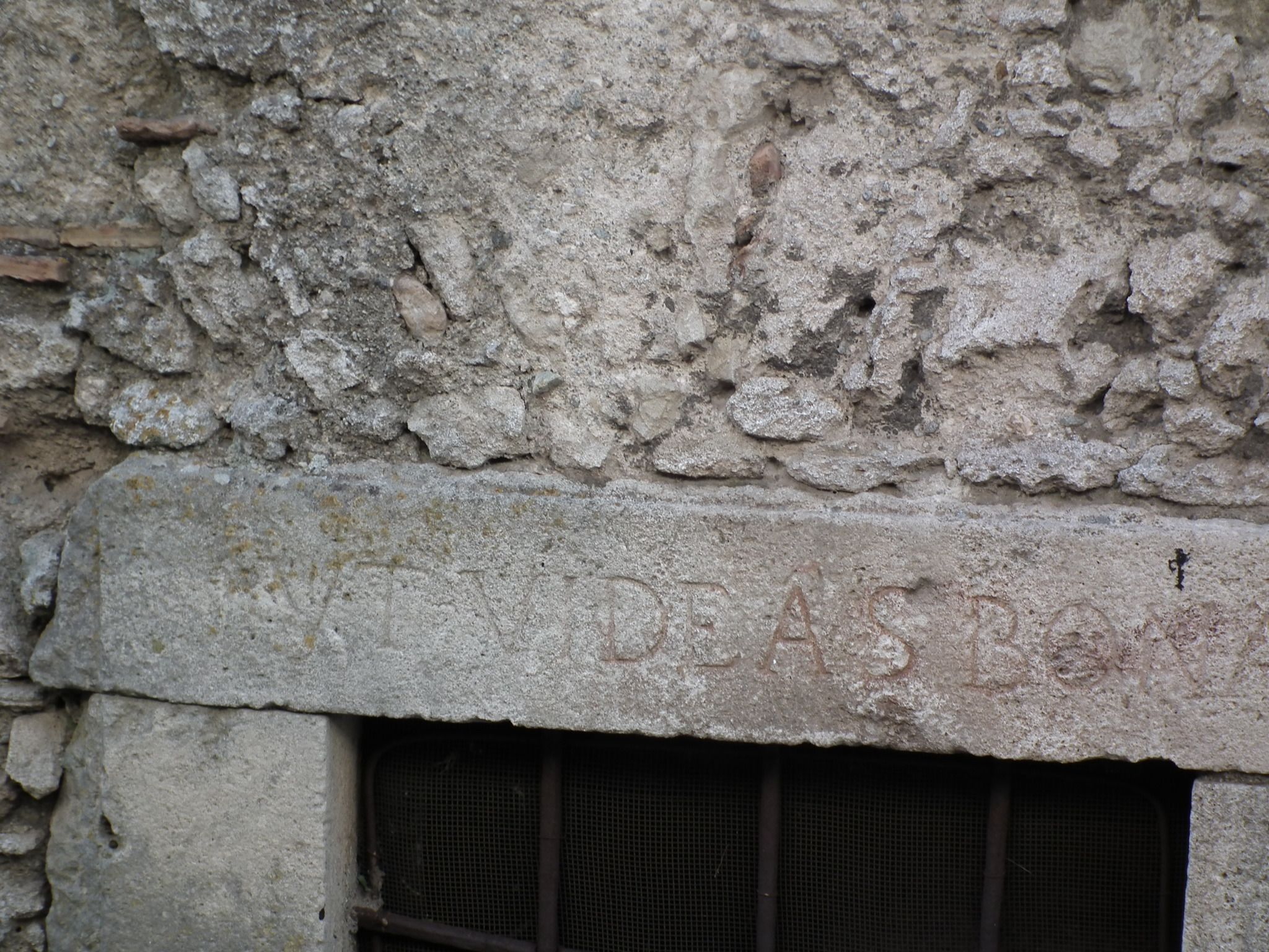 A stone wall with a window featuring a metal grille.