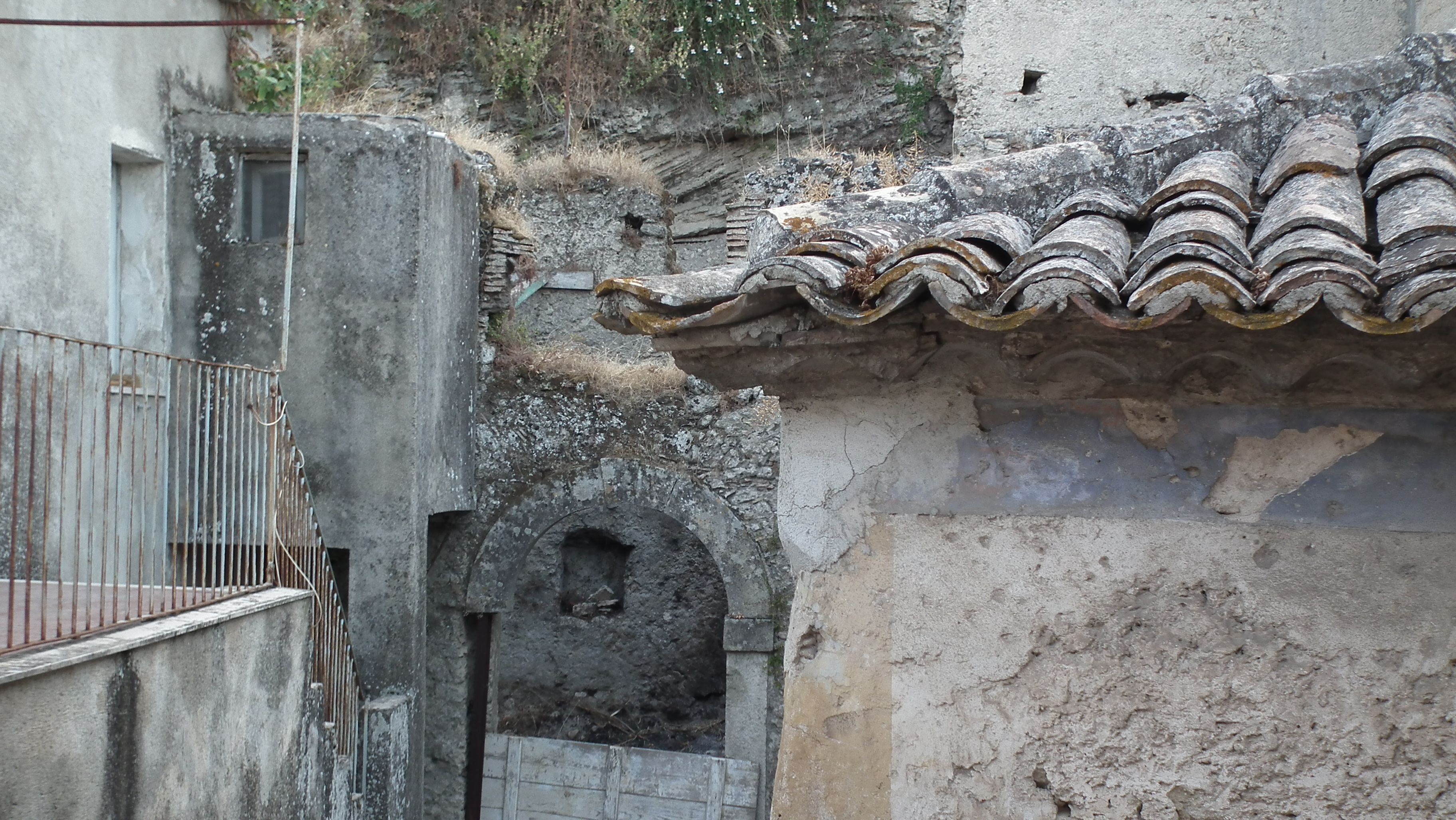 Un edificio de piedra encallecido, con una verja metálica y una pequeña entrada arqueada.