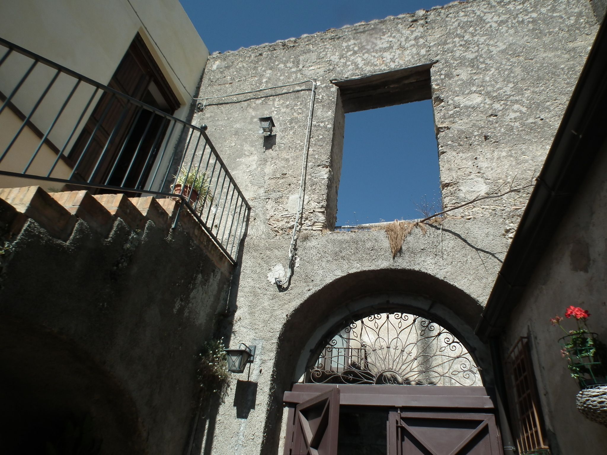 Un pasaje arqueado con una reja de metal, una pequeña ventana y un balcón con barandilla.