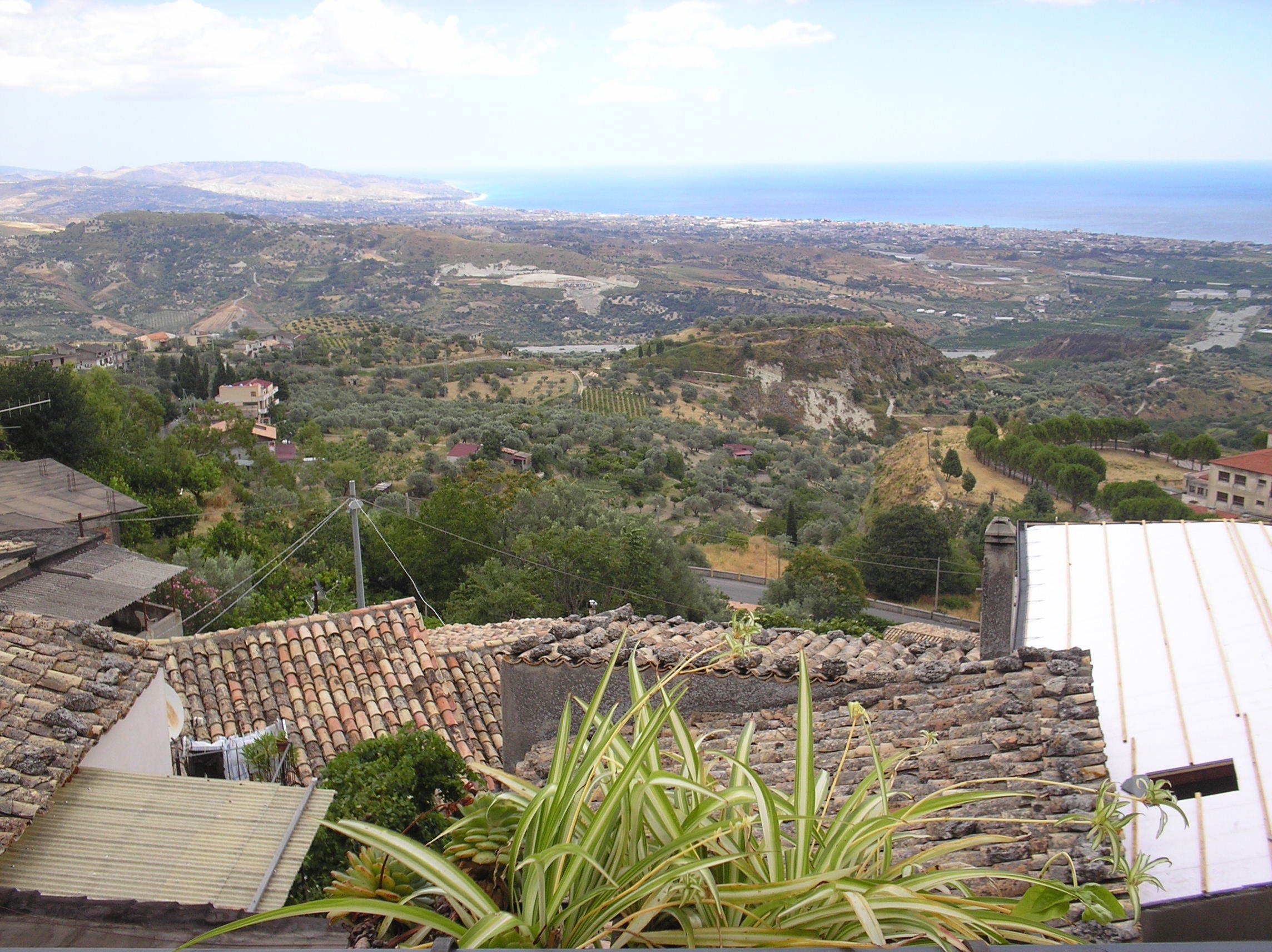 Vista da una terrazza sul tetto su un paesaggio costiero con campi a gradoni e un mare in lontananza.