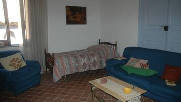 Una habitación con un sofá azul, una cama pequeña con ropa de cama estampada, una mesa de madera con un cuenco y un libro, y un cuadro en la pared.