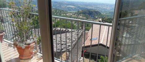 Un balcón con planta en maceta, suelo de baldosas y vista a un paisaje distante.