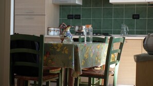 Une cuisine avec des carreaux verts, des armoires en bois et une table recouverte d’une nappe à motifs floraux.