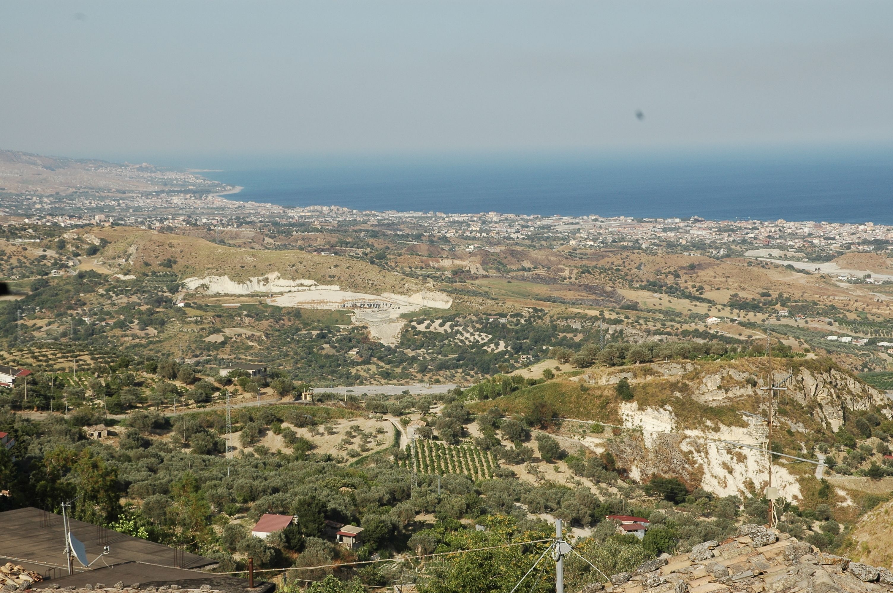 Ein weiter Panoramablick auf eine Küstenstadt mit einem markanten Hügel, einem kleinen Dorf und freiem Blick auf das Meer.
