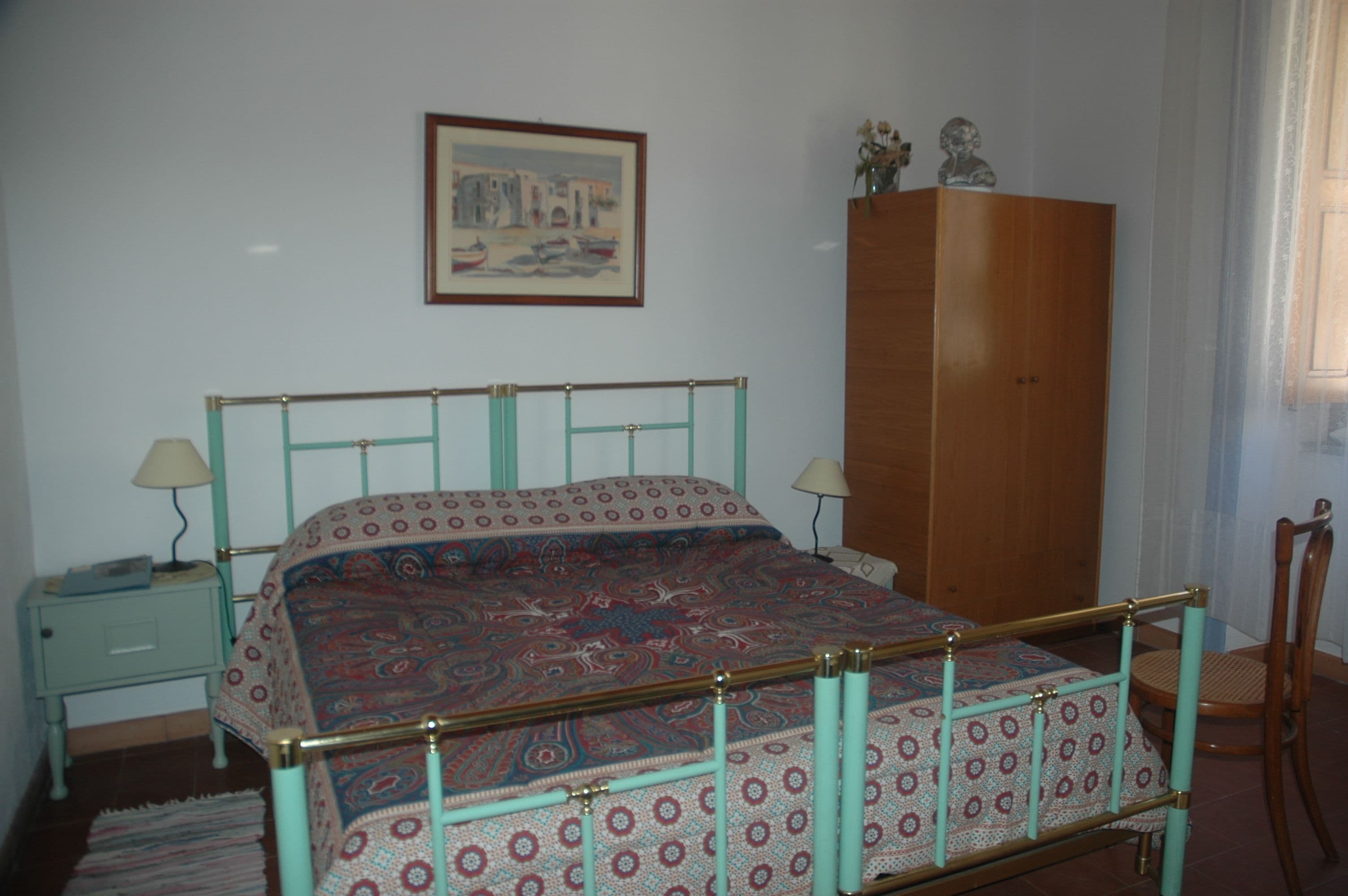 Une chambre à coucher avec un lit, des tables de chevet, une armoire en bois et un tableau encadré au mur.