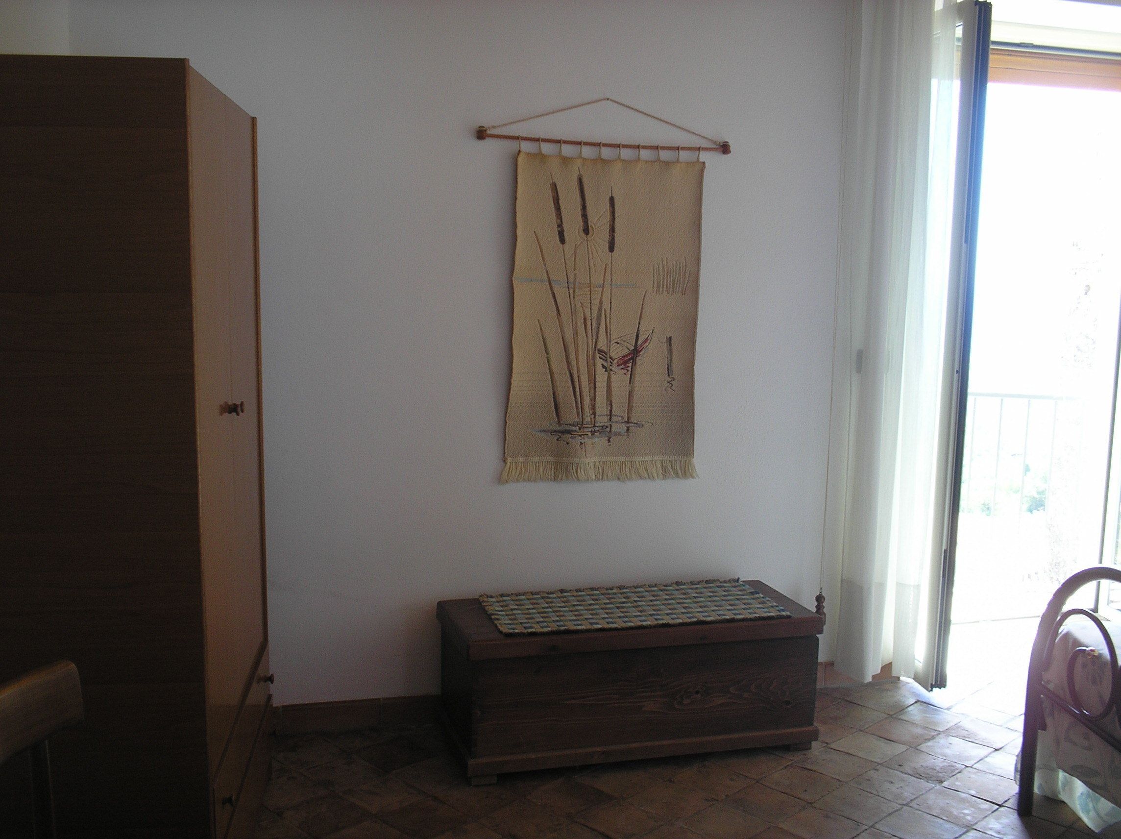 Una habitación con un armario de madera, un banco tejido y un tapiz que representa juncos.