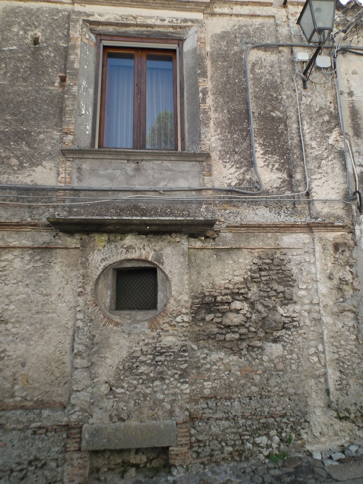 Une façade de bâtiment usée par les intempéries, avec une fenêtre et une petite fenêtre circulaire.