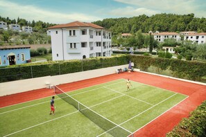 Un court de tennis avec un filet, entouré d’une clôture et de verdure.
