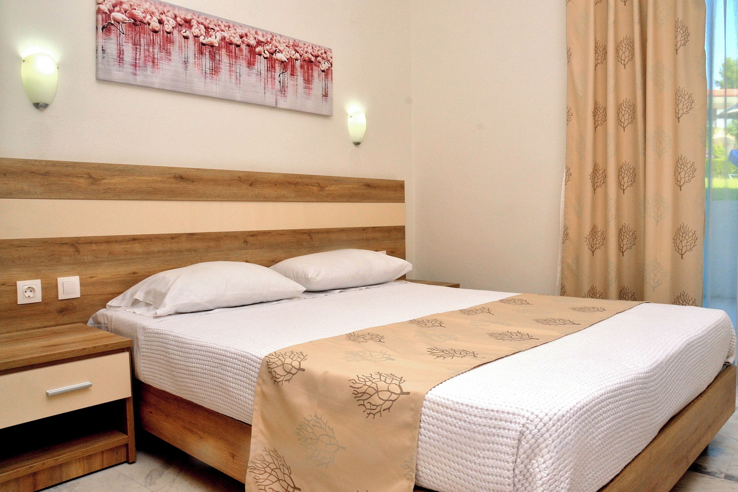 A neatly made bed with a beige bedspread, a wooden headboard, and two bedside tables with lamps.