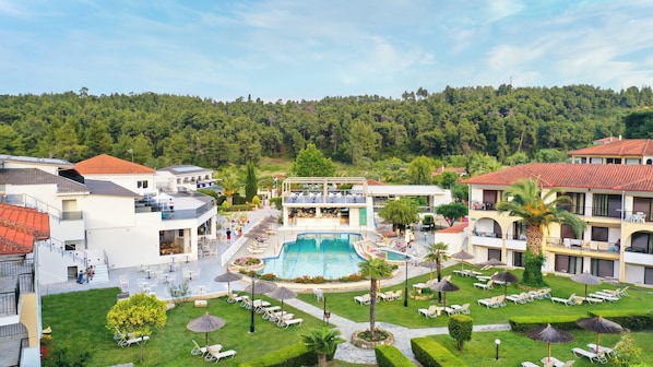A resort with a central swimming pool, outdoor seating, and a view of a forested hillside. - Chrousso Village (Kassandra)