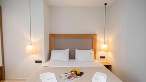 A hotel room with a neatly made bed, two bedside lamps, and a magazine on the bed. - Chrousso Village (Kassandra)