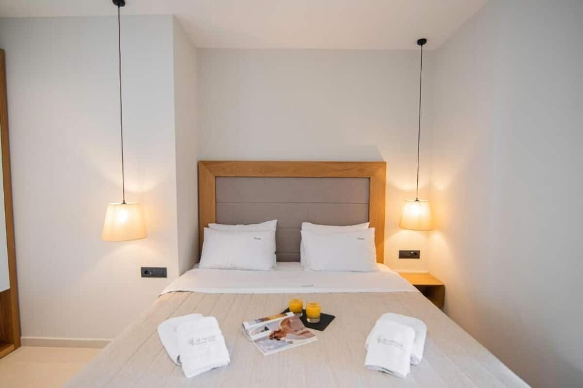 A hotel room with a neatly made bed, two bedside lamps, and a magazine on the bed.