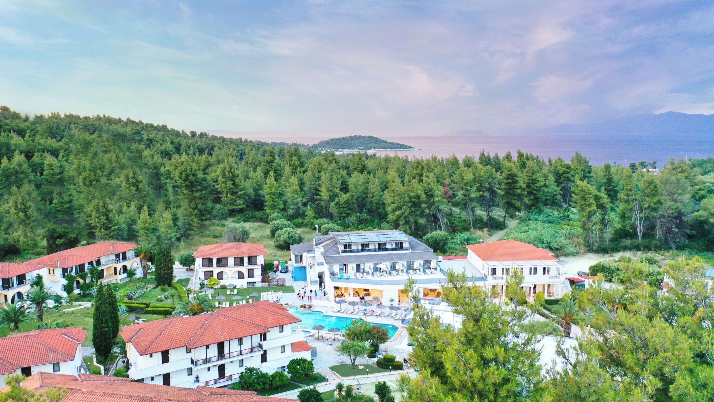 A resort with multiple buildings, a swimming pool, and a forested backdrop.