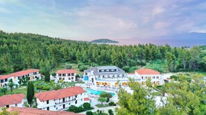 Ett semesterområde med flera byggnader, en swimmingpool och en skog som utgör bakgrunden.