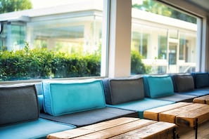 Une rangée de bancs en bois avec des coussins, un mur de verre et une vue sur la verdure à l’extérieur.
