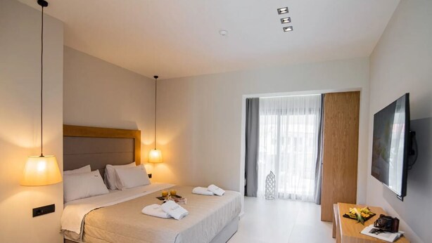 A modern hotel room with a large bed, bedside lamps, a wooden desk, and a TV on the wall. - Chrousso Village (Kassandra)