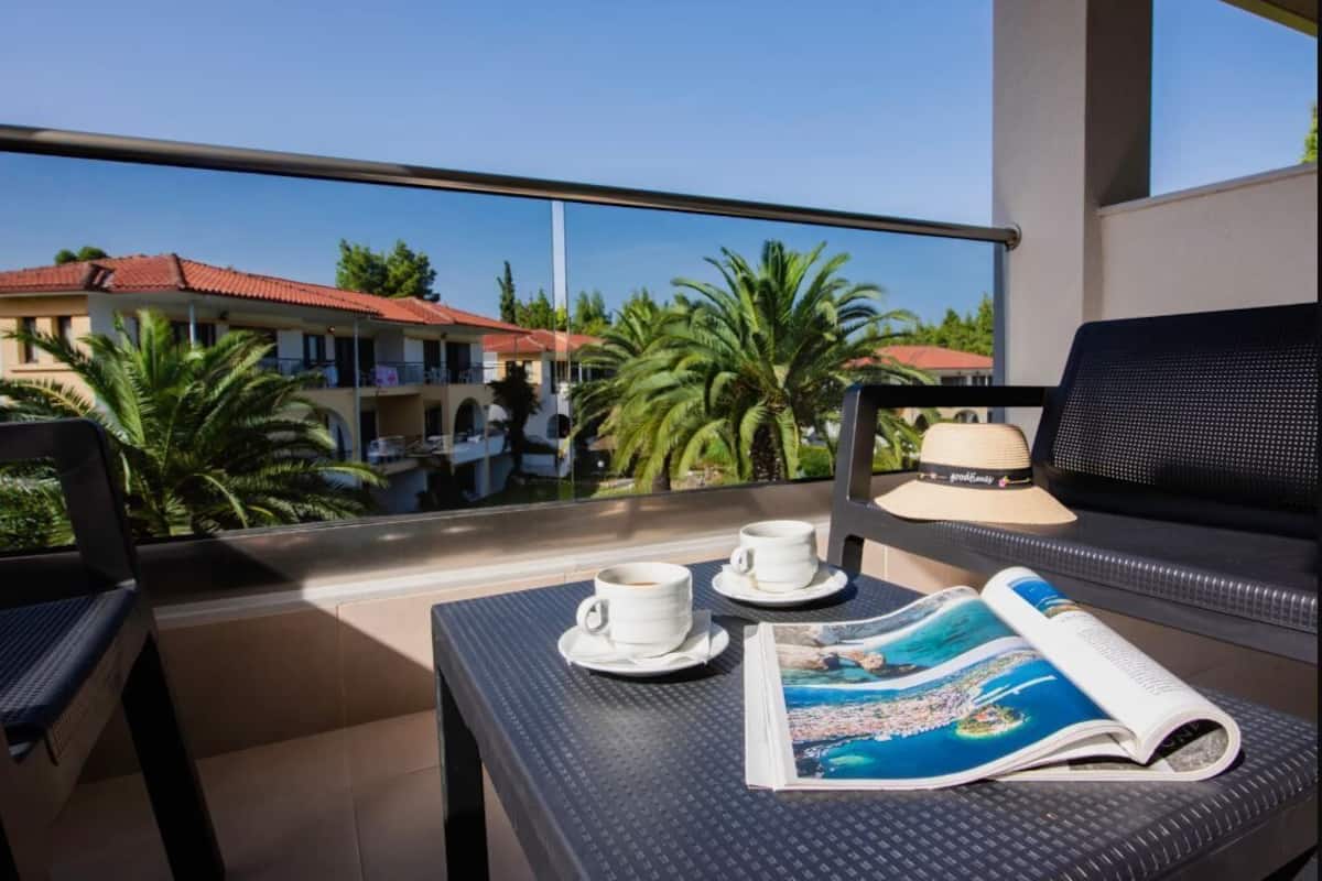 A balcony with two white cups and saucers, a magazine, and a hat on a table.