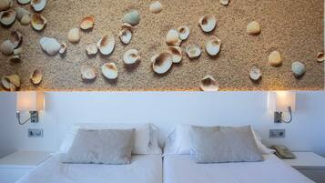 Habitación de hotel con una cama, dos almohadas y una pared decorada con conchas marinas.