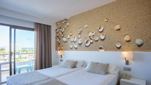 A hotel room with two beds, a large window with curtains, a wall decorated with seashells, and a view of the city. - BQ Can Picafort Hotel (Santa Margalida)