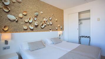 Un dormitorio con una cama, dos mesitas de noche, un estante en la pared con conchas decorativas, una lámpara de pared y un armario con un tendedero.