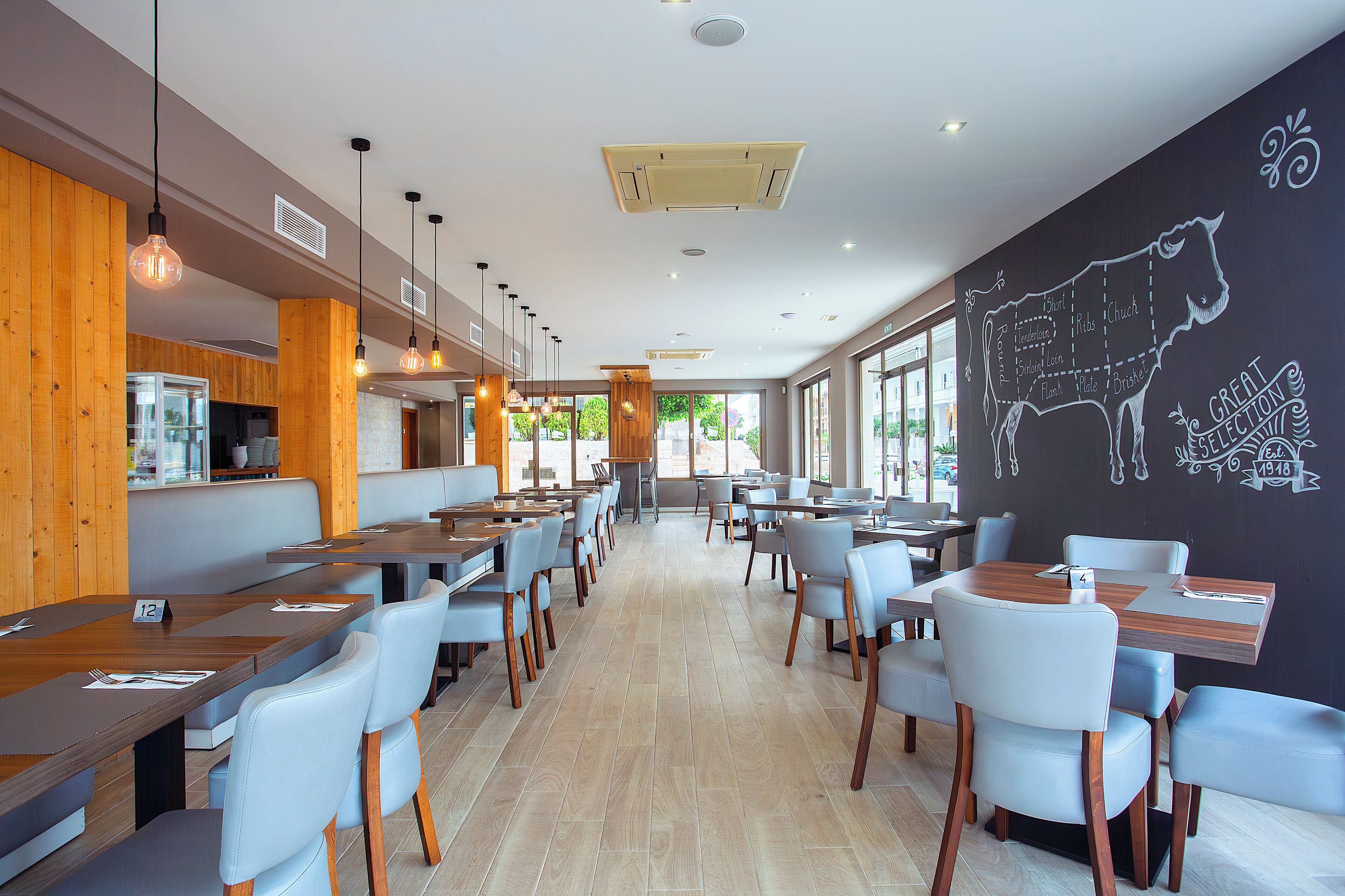 Un restaurant moderne avec des éléments décoratifs en bois, plusieurs espaces de restauration et un mur noir où est dessinée une vache.