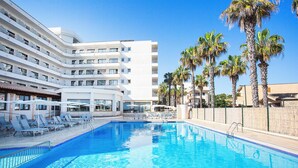 A swimming pool with lounge chairs and umbrellas, surrounded by palm trees and a multi-story building with balconies. - BQ Can Picafort Hotel (Santa Margalida)