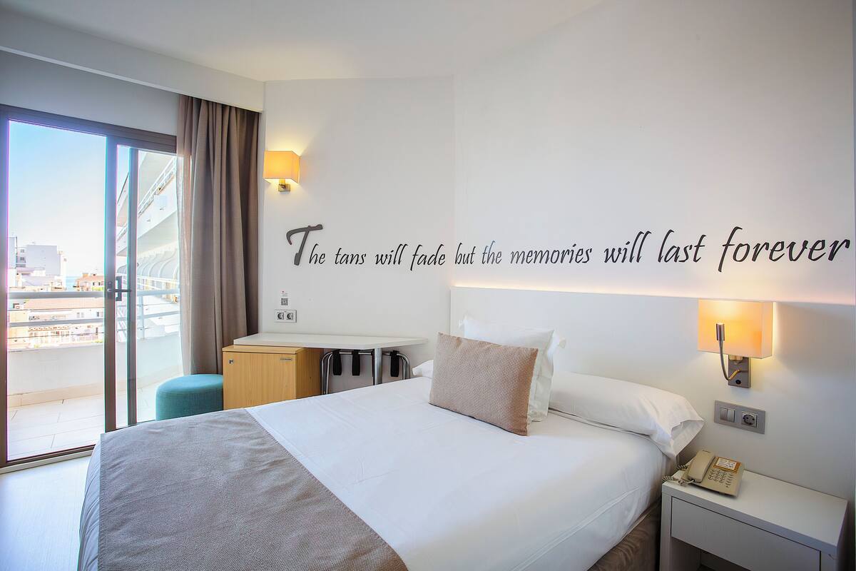 A hotel room with a large bed, a desk, and a view of the city through the window.