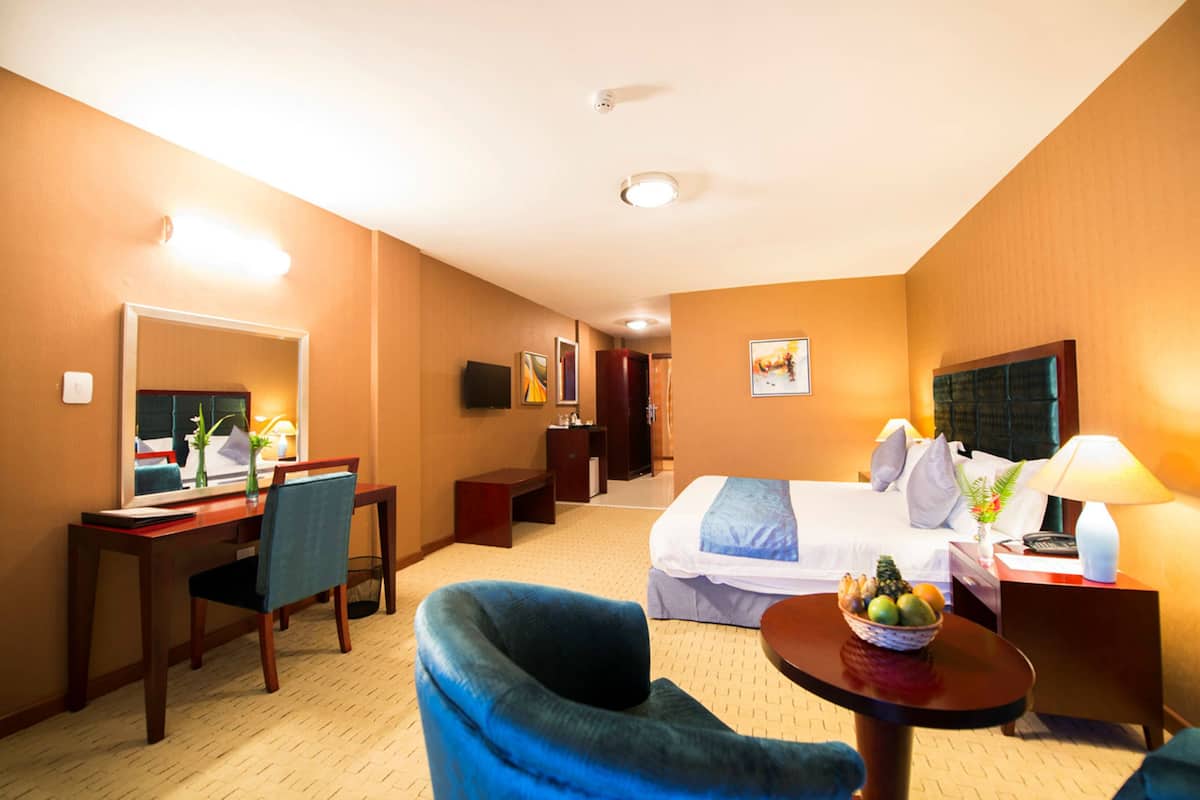 A hotel room with a bed, desk, chair, and a small table with a fruit bowl.