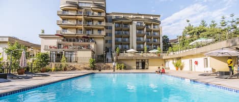 Un hotel de varios pisos con piscina, mobiliario exterior y balcones.