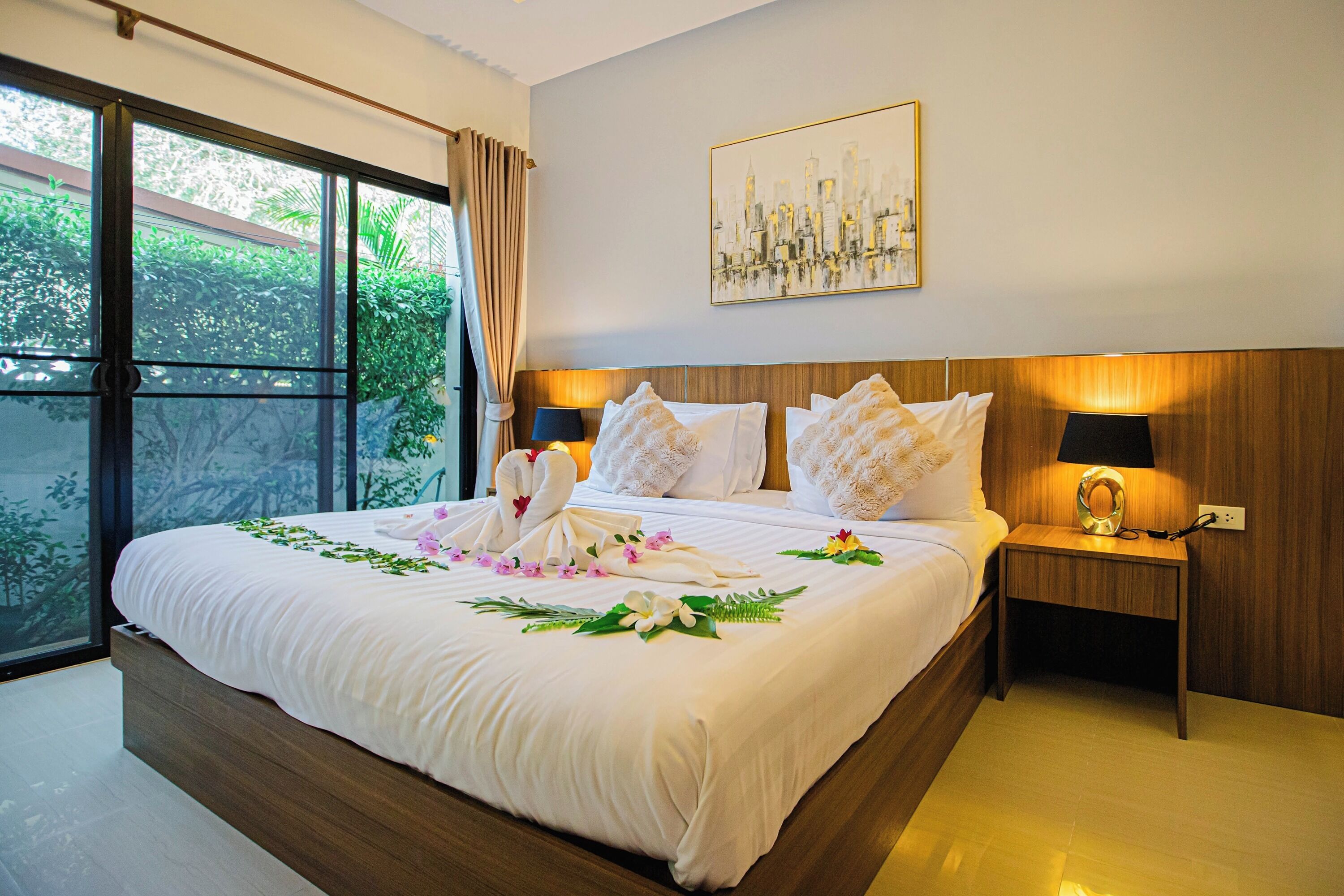 A neatly made bed with floral decorations, a cityscape painting, and a nightstand with a lamp.
