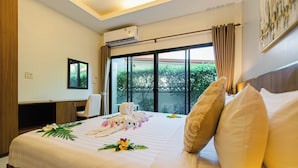 A hotel room with a large bed, a desk, a chair, and a view of greenery through the window. - Happy Eight Resort (Rawai)