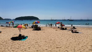 A beach with people sunbathing and swimming, umbrellas, and boats in the water. - Happy Eight Resort (Rawai)