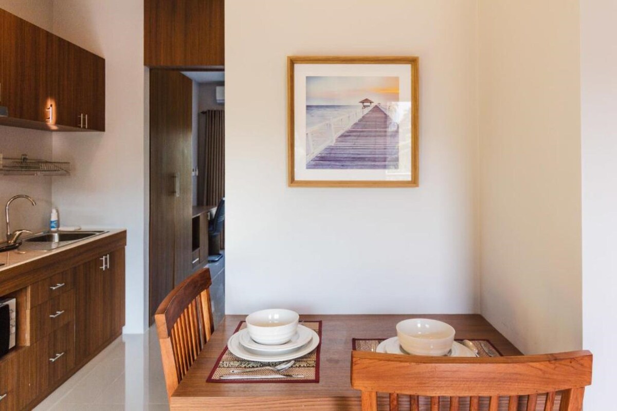 A dining area with a wooden table set for two, a framed picture on the wall, and wooden cabinets.