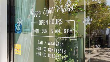 A window with a sign indicating 'Happy Eight Phuket' and 'OPEN HOURS MON-SUN 9 AM-6 PM'.