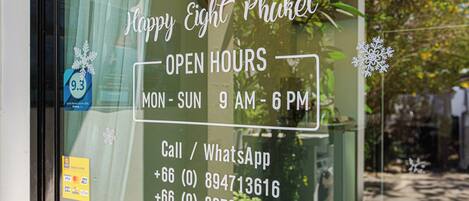 A window with a sign indicating 'Happy Eight Phuket' and 'OPEN HOURS MON-SUN 9 AM-6 PM'.