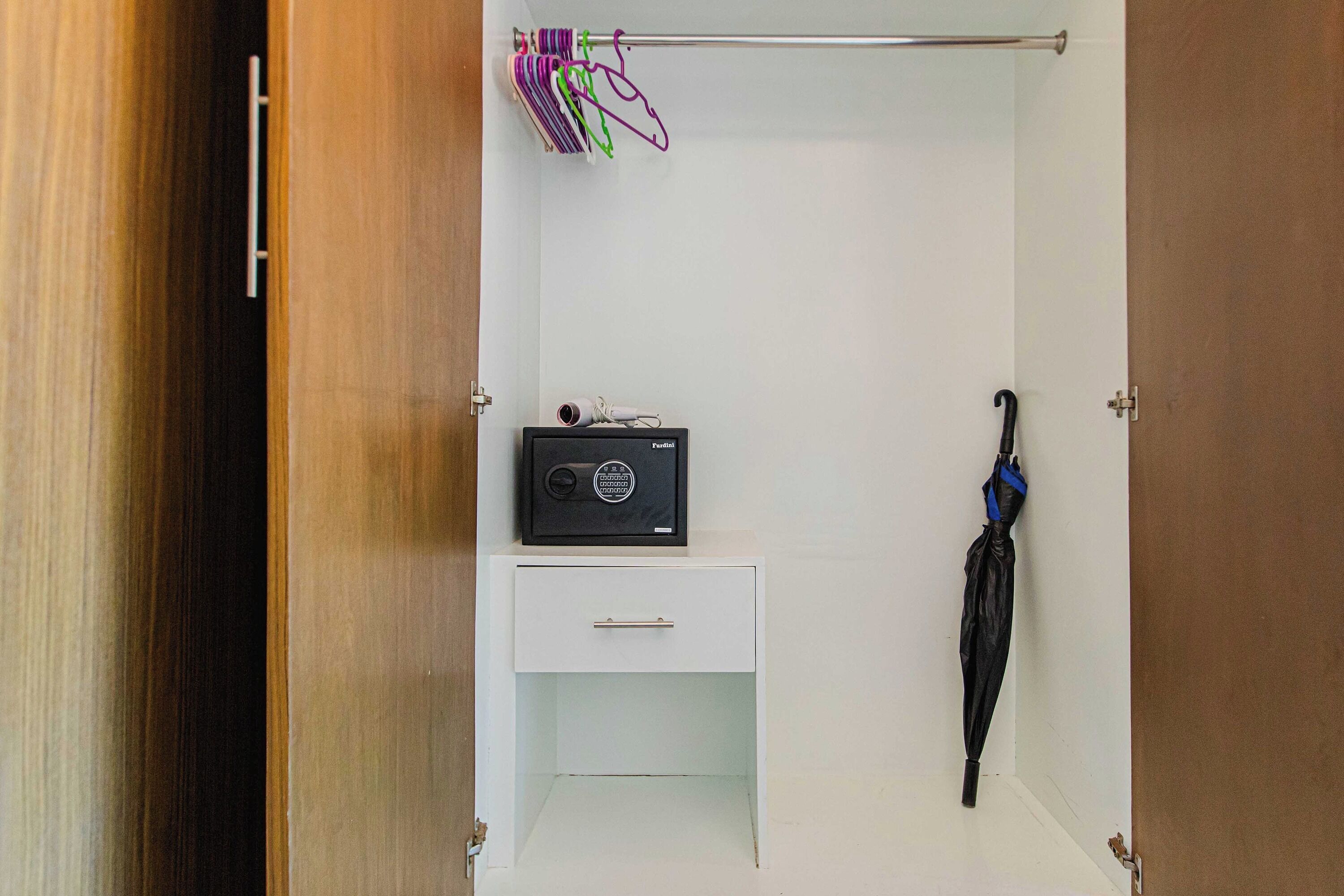 Une pièce avec un mur blanc, une porte en bois, un meuble blanc contenant une radio, et un parapluie noir accroché au mur.