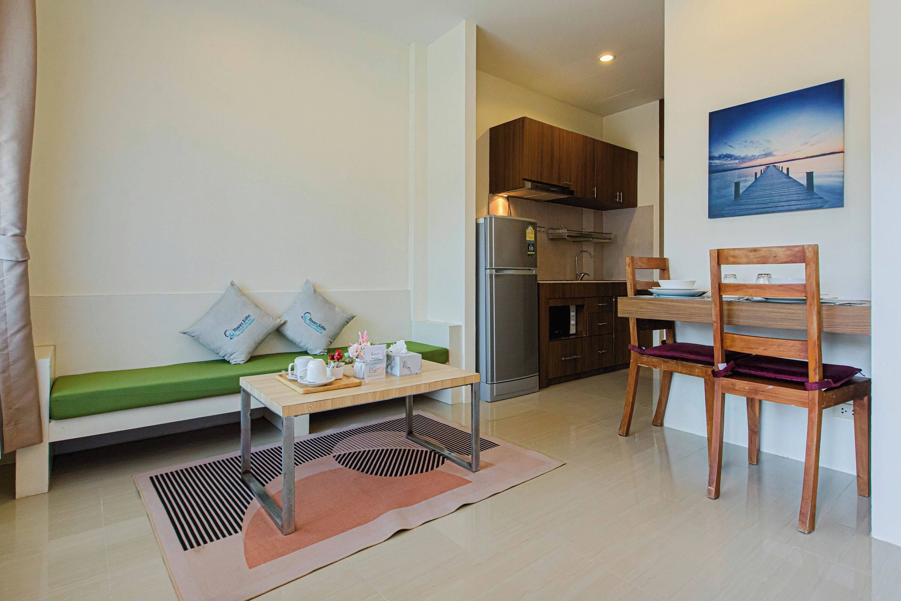 A compact living space with a kitchenette, a dining area with a table and chairs, a sofa with cushions, and a painting on the wall.