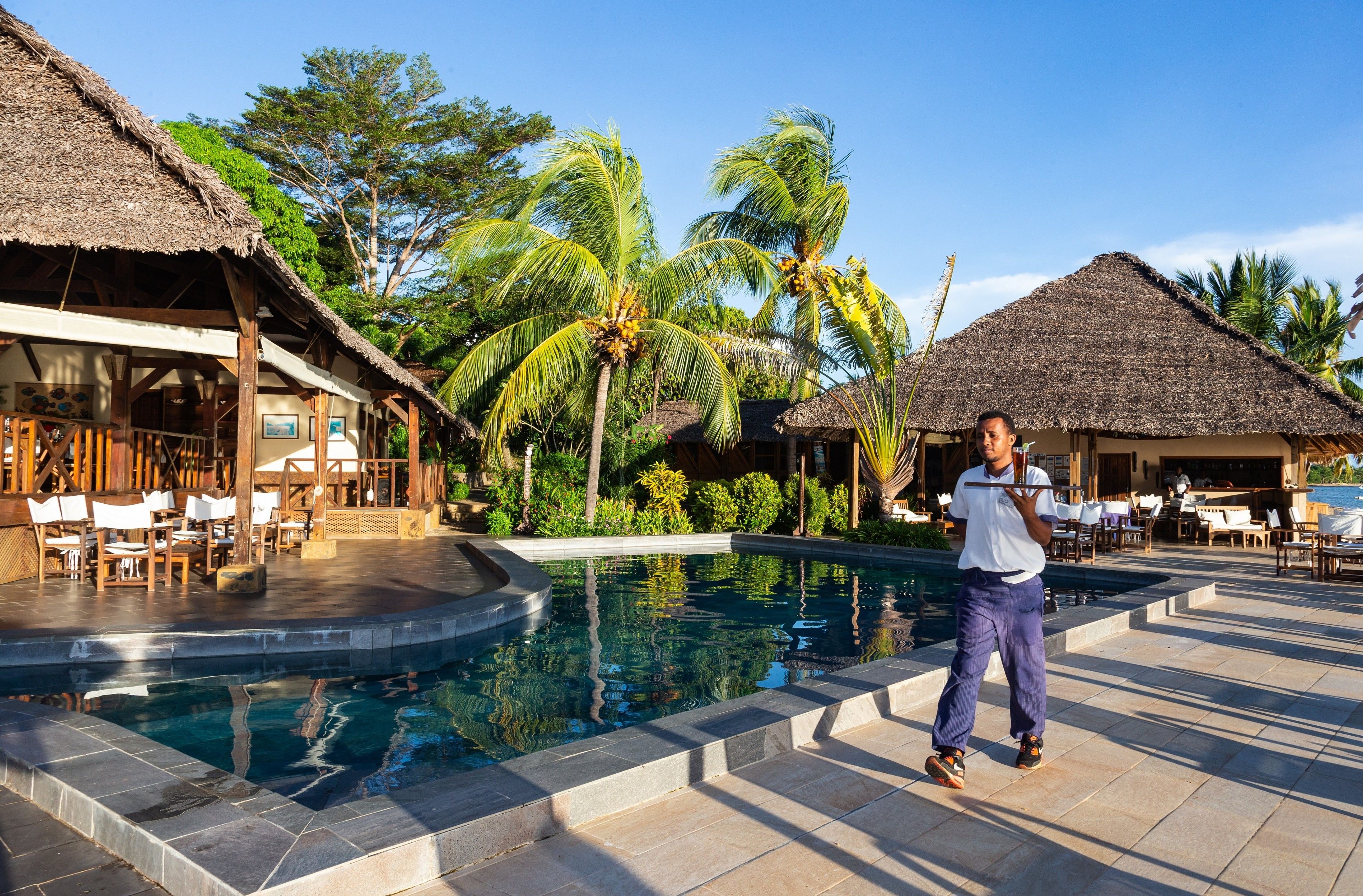 A pool area with a thatched-roof structure, lounge chairs, and palm trees.