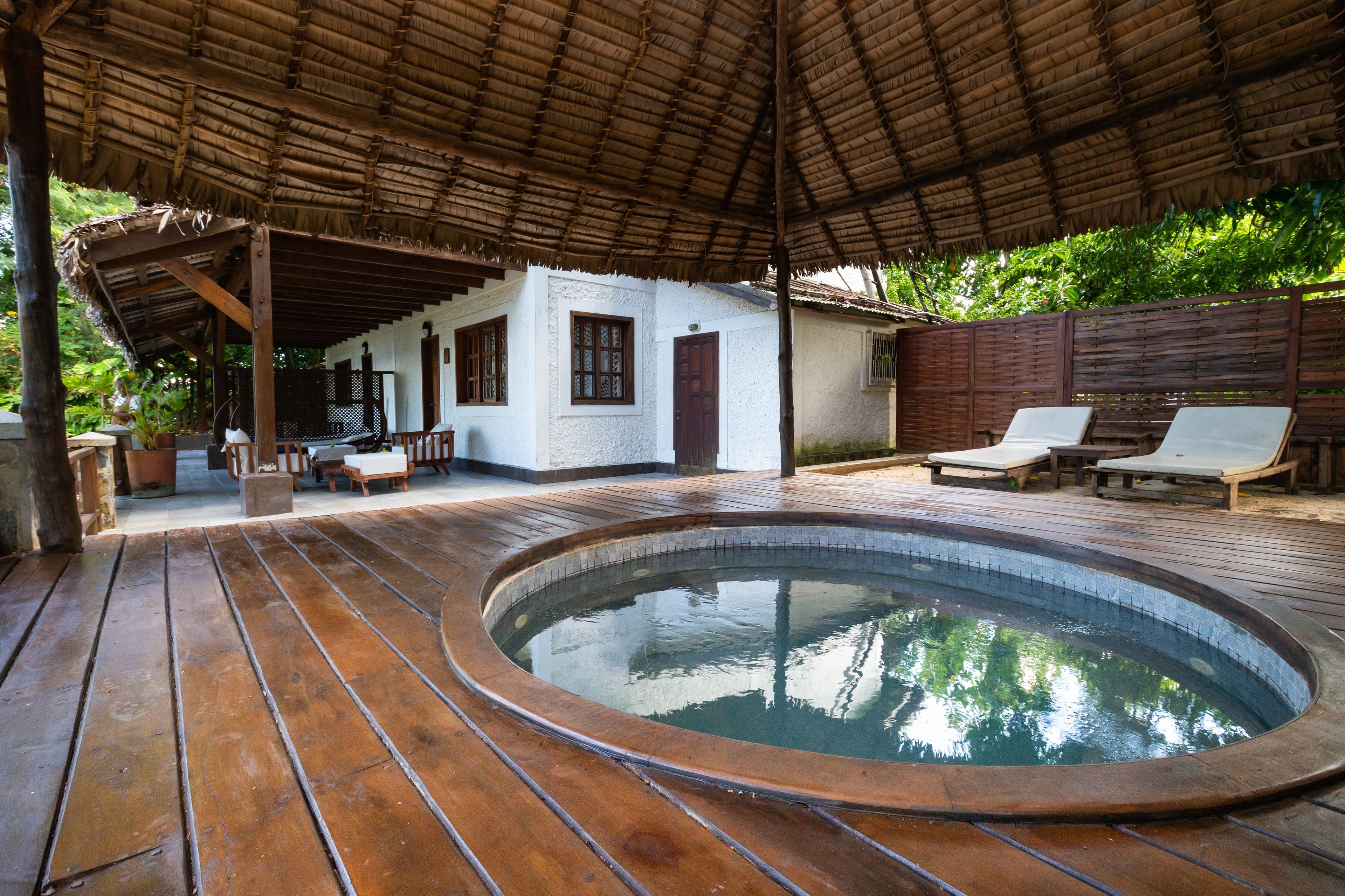 Eine Holzterrasse mit Whirlpool, ein überdachter Patio und ein weißes Gebäude mit Fenstern und einer Tür.